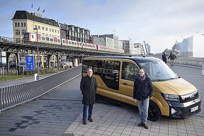 Ein Kleinbus mit zwei Personen vor der Kulisse der Hamburger Hochbahn